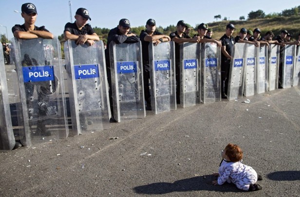 epa04937948 A Syrian refugee baby plays in front of riot police at the Istanbul-Edirne highway as they wait for permission to pass Turkish Greek border to reach Germany in Edirne, Turkey 19 September 2015. Turkey has spent 7.6 billion US dollar on caring for 2.2 million Syrian refugees since the civil war began in 2011, Deputy Prime Minister Numan Kurtulmus said on 18 September. Turkey hosts more Syrians who fled their homeland than any other country. Most Syrians, however, have no legal right to work and rights groups report housing remains a huge issue for many.  EPA/TOLGA BOZOGLU  EPA/TOLGA BOZOGLU
